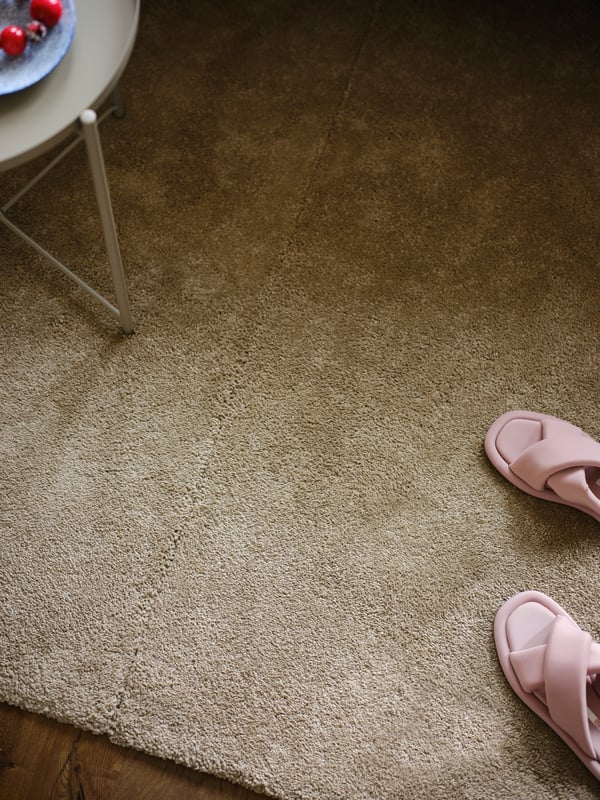 Two off-white STOENSE low pile rugs placed together with a pair of pink slippers and a GLADOM tray table on top.