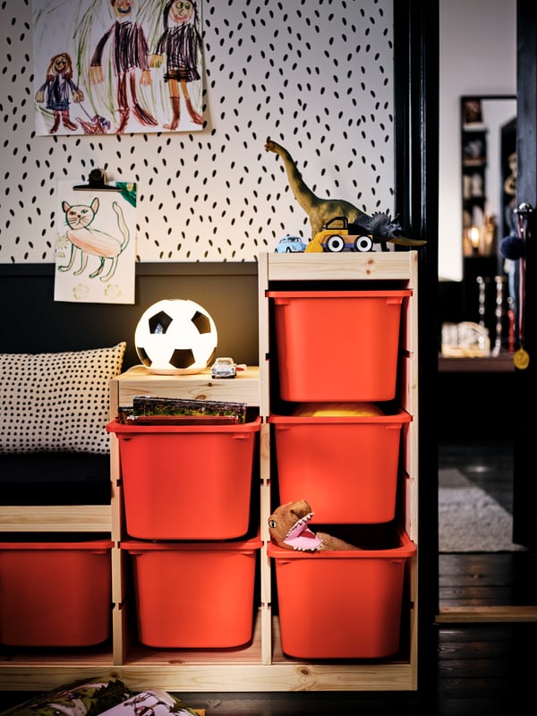 Un rangement TROFAST avec des bacs de rangement oranges se démarque dans une chambre entièrement noire et blanche.