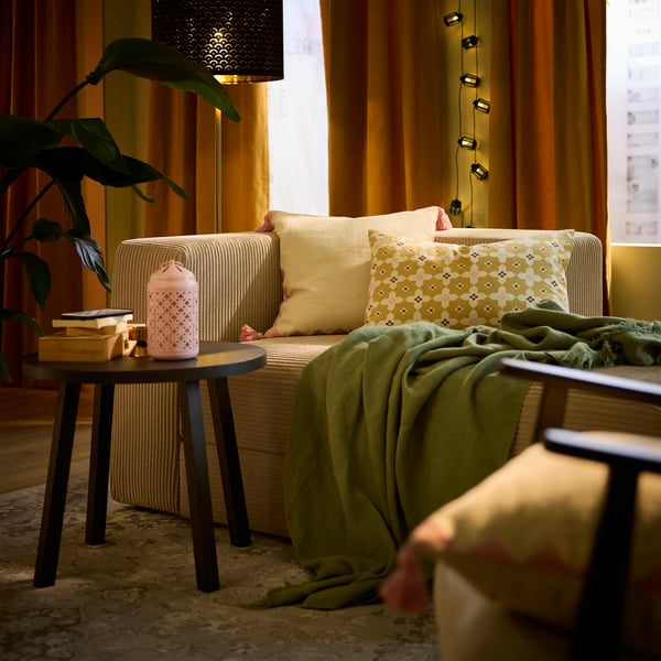 Two multicoloured GOKVÄLLÅ cushion covers rest on a sofa, accompanied by a throw, in a cosy living room.