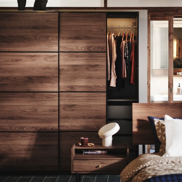 Une chambre à coucher avec une commode et une table de chevet RÅDMANSÖ, ainsi qu'une armoire PAX MEHAMN à l'arrière-plan. Le tout en bois foncé.