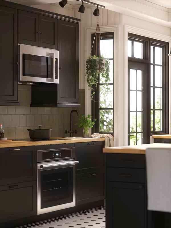 A kitchen with black-stained LERHYTTAN fronts has kitchen appliances in black and stainless steel and a black sink.
