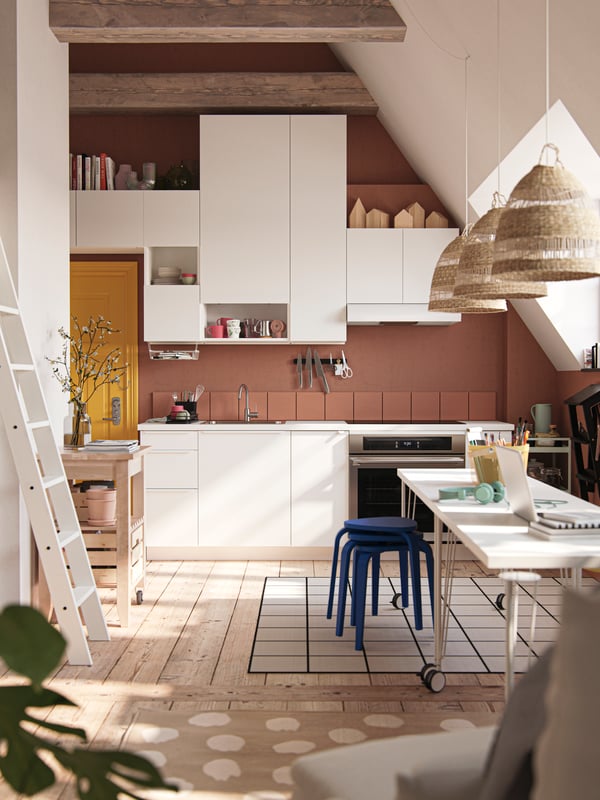 A studio apartment with sloped walls, large windows, dark walls, yellow front door and white VALLSTENA kitchen fronts.