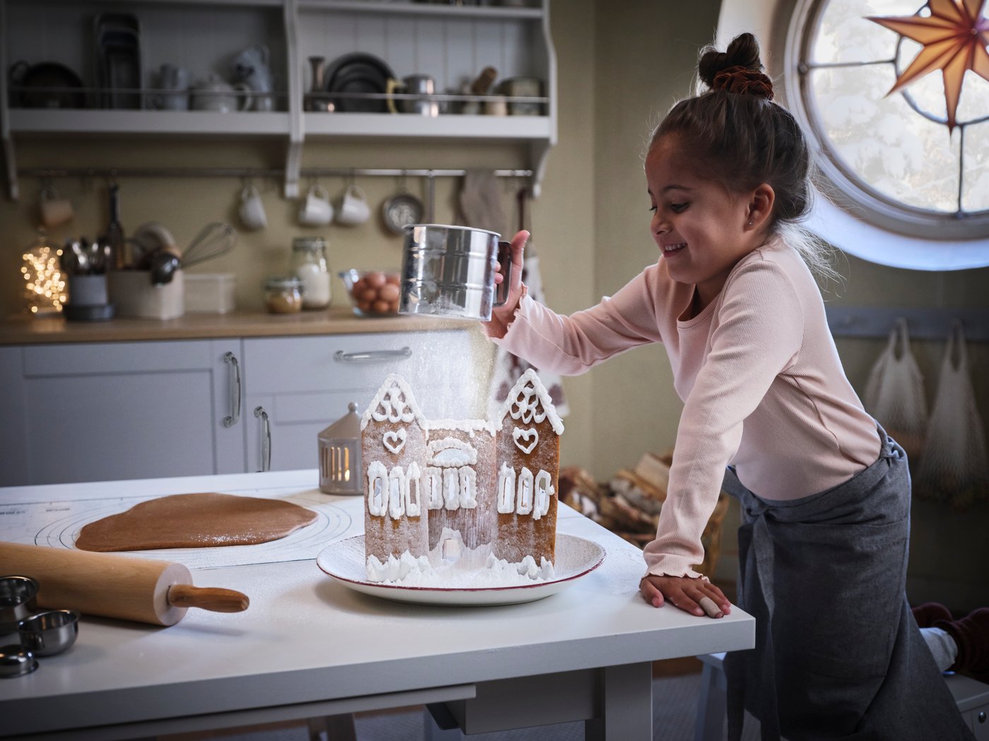 Ett barn pudrar ett pepparkakshus med en IDEALISK mjölsikt.