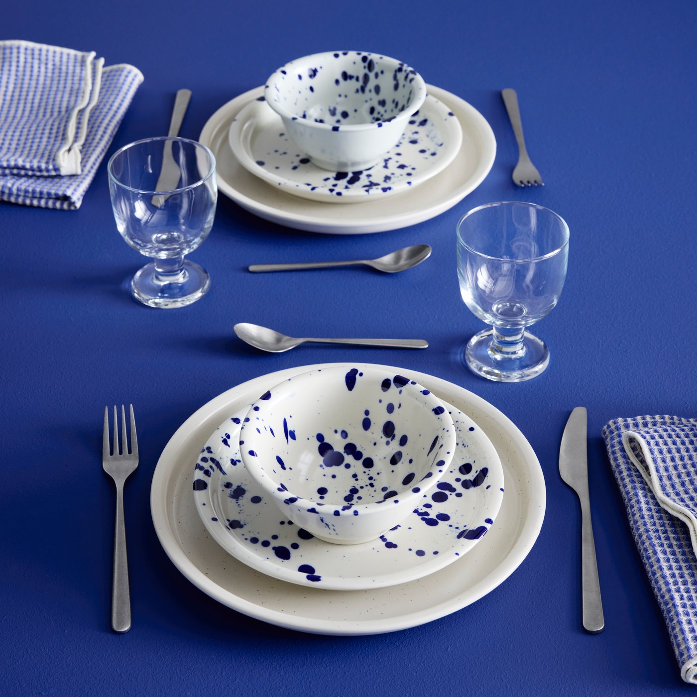 A table setting features blue patterned SILVERSIDA bowls, white plates, glasses and utensils all arranged on a blue surface.