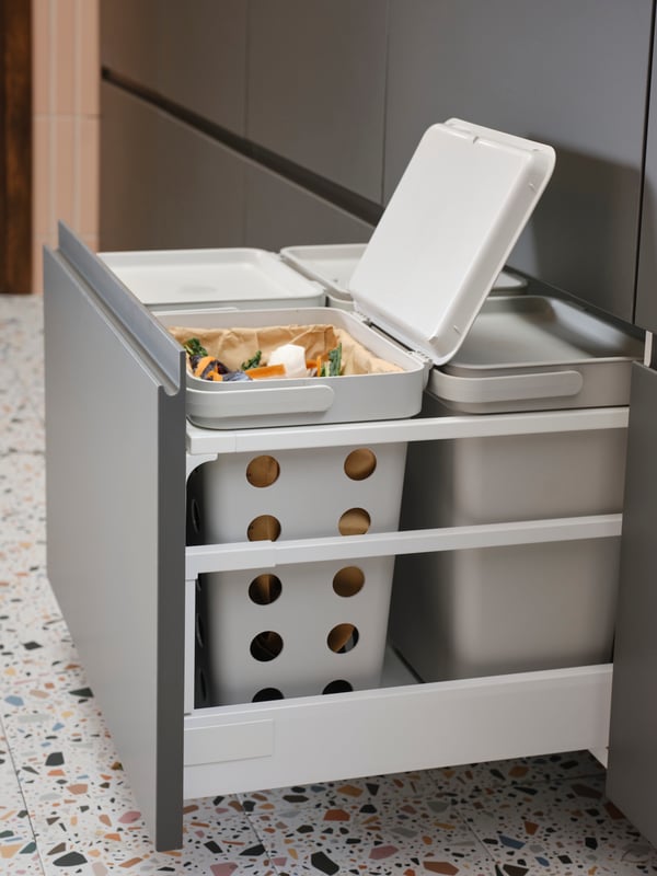 A light grey HÅLLBAR waste sorting solution inside a kitchen drawer in a kitchen with dark grey drawer fronts.