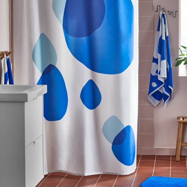 A white and blue BERGVATTNET shower curtain is covering a shower space with bath towels hanging on hooks on a wall beside it.