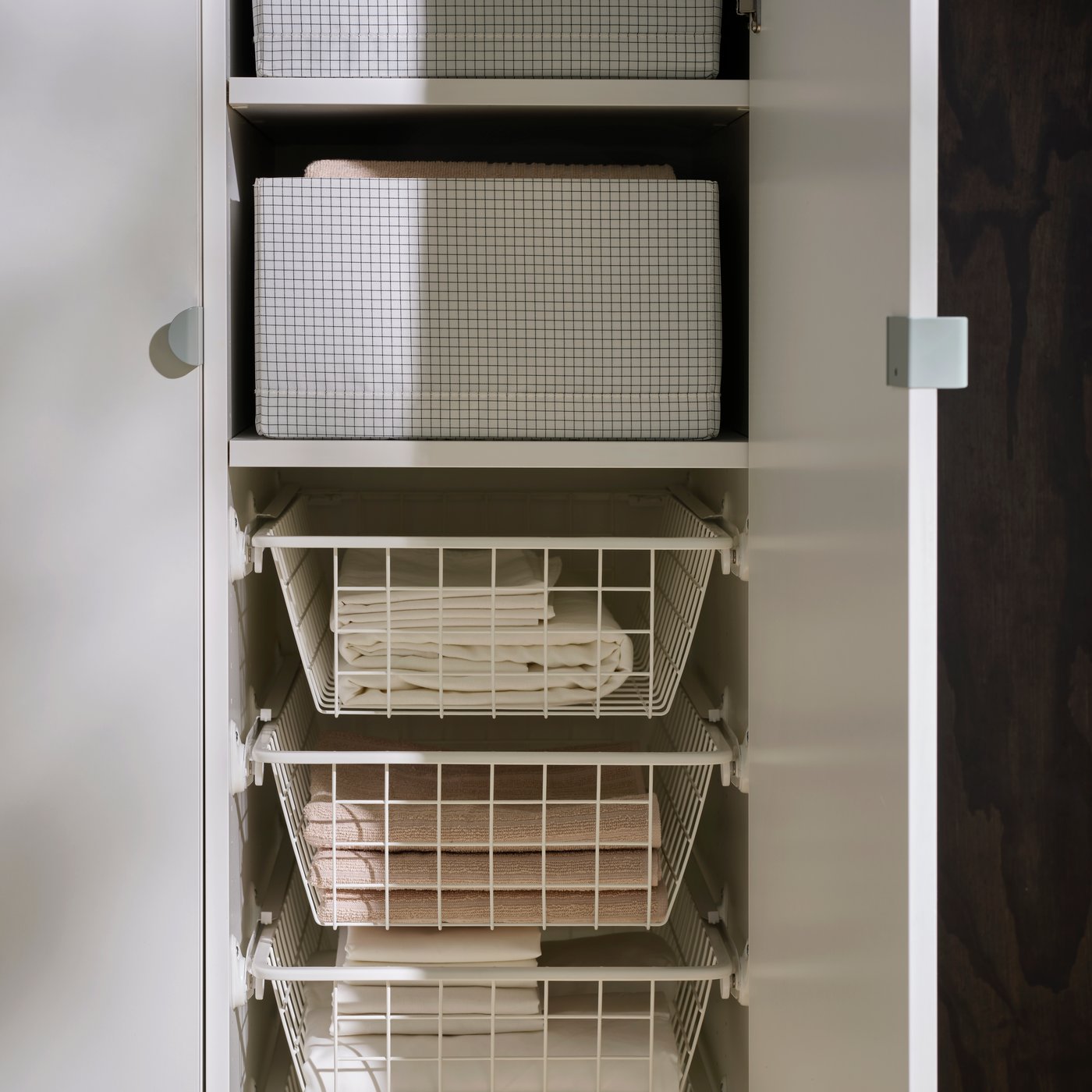 Inside a LASTARE wardrobe combination with STUK boxes on shelves and wire baskets storing neatly folded textiles.
