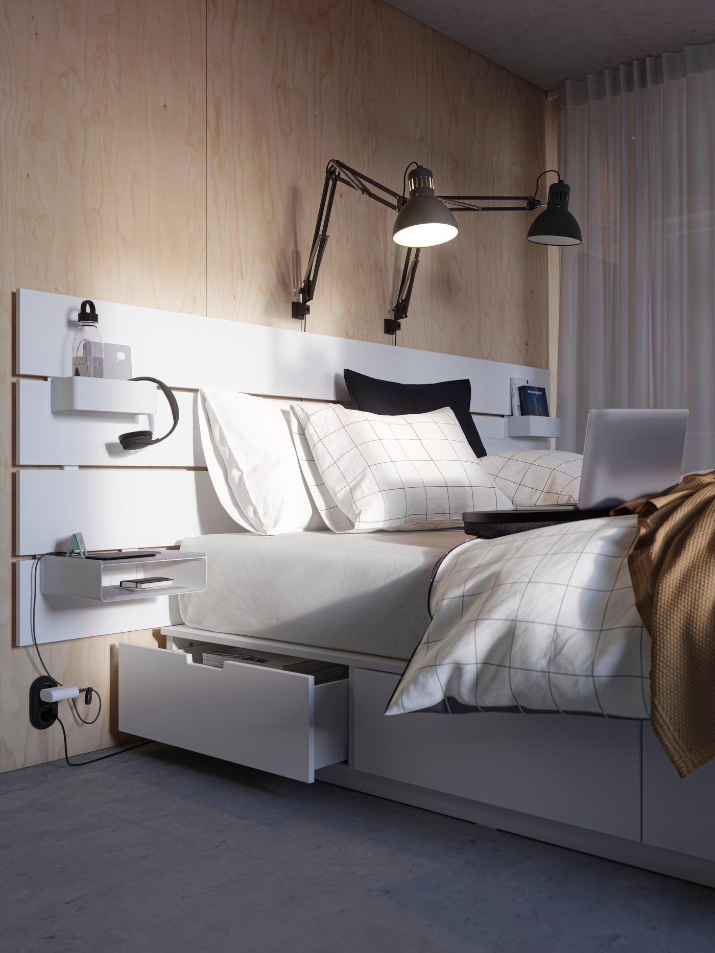 Es ist ein weißes NORDLI Bettgestell mit Schubladen und Kopfteil zu sehen. Eine Schublade ist geöffnet. Am Kopfteil sind TERTIAL Arbeitsleuchten angebracht, wovon eine eingeschaltet ist.