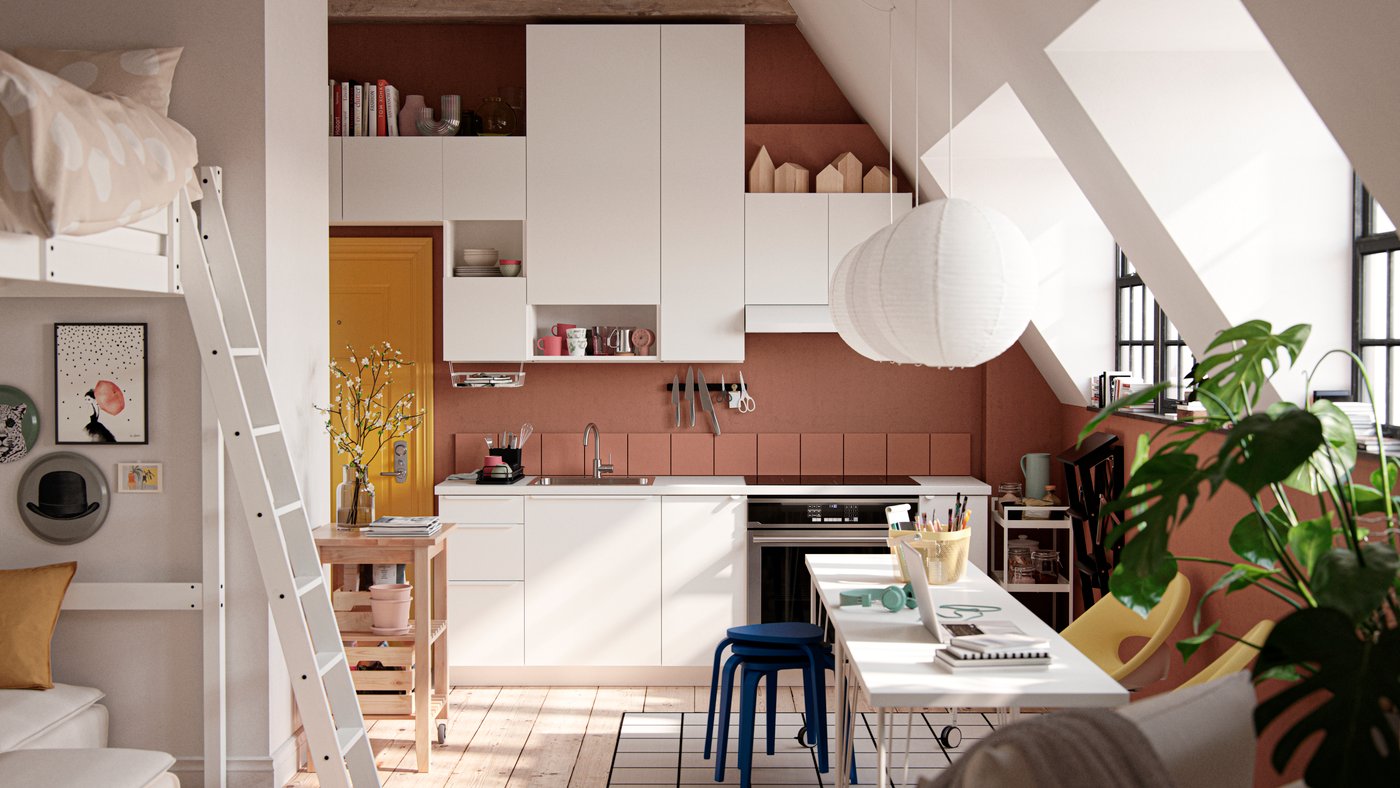 A studio apartment with large industrial-style windows, dark terracotta-coloured walls and white VALLSTENA kitchen fronts.