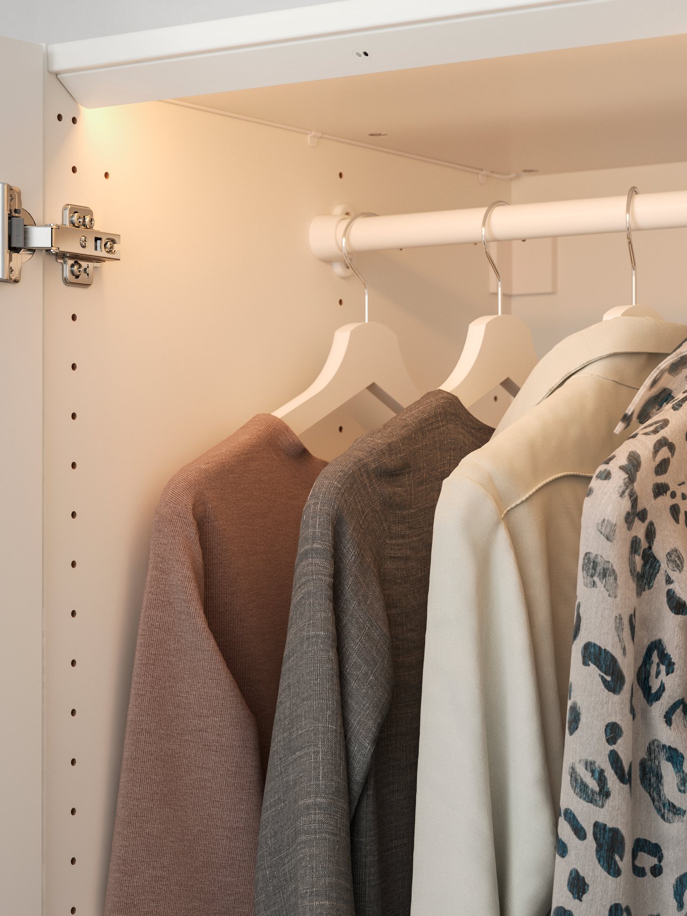 ÖVERSIDAN PAX wardrobe integrated lighting shining light on a white clothes rail with clothing items hanging neatly with BUMERANG hangers. 