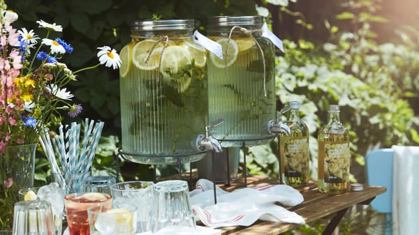 A small garden table set with glasses, straws, and lemonade in a VARDAGEN jar with tap, ready for guests at a party.