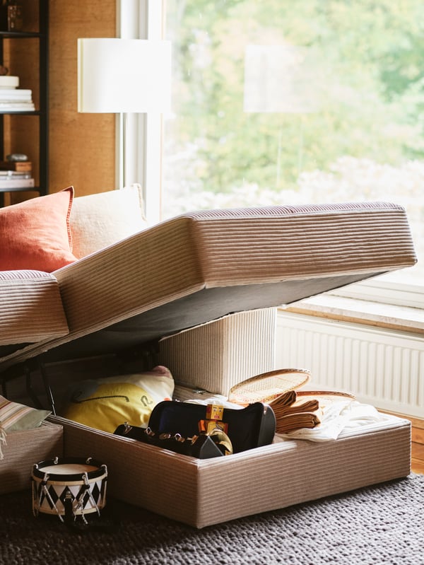 Sunlit through a nearby window is the chaise longue of a grey-beige JÄTTEBO sofa, seating raised to reveal storage within.