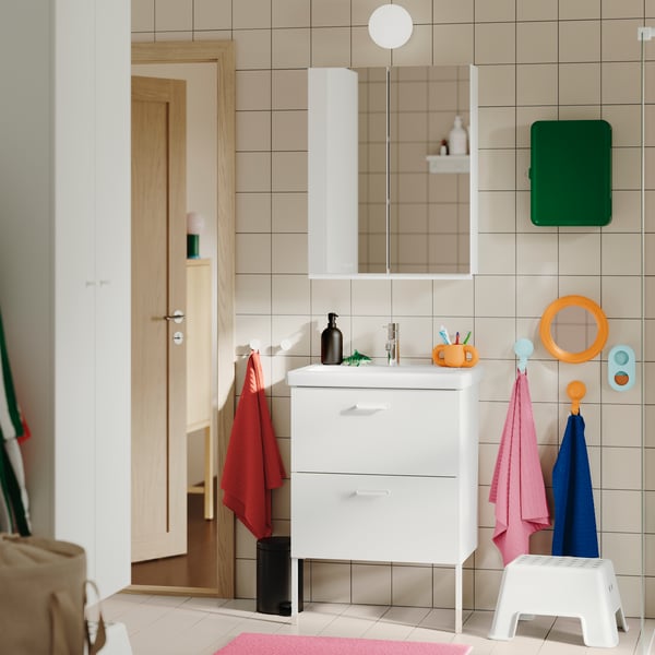 A tiled bathroom featuring the white TVÄLLEN/ENHET wash-stand with two drawers, wall-mounted with colourful towels nearby.