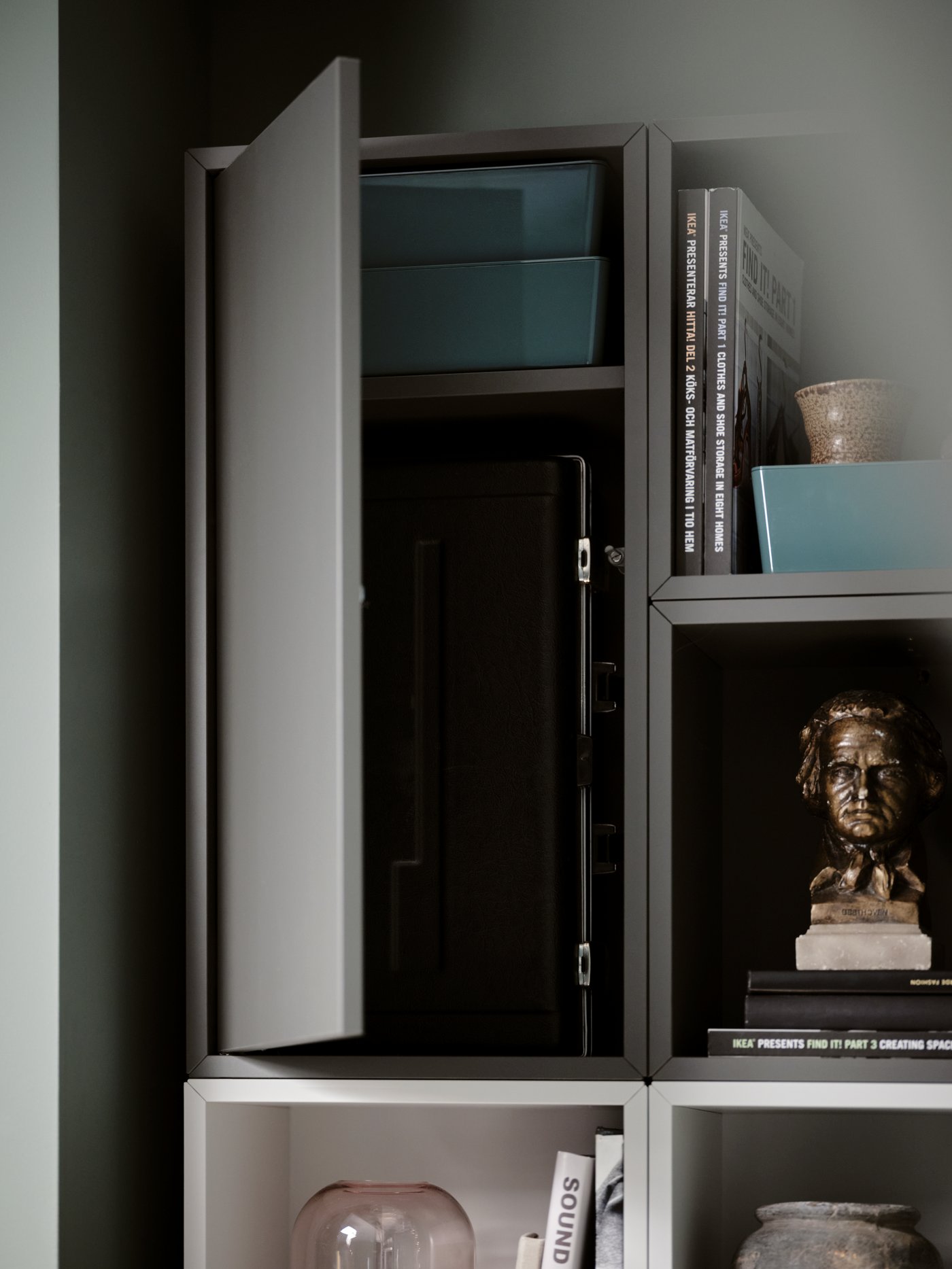 Open and closed storage – books, decorations, and more – made up of a combination of dark-grey and white EKET cabinets.