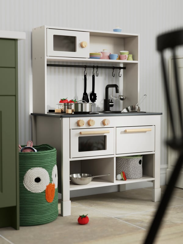 Une cuisine pour enfants SILLTRUT, de couleur grise claire, comporte des poêles, des casseroles et d’autres ustensiles de cuisine empilés.