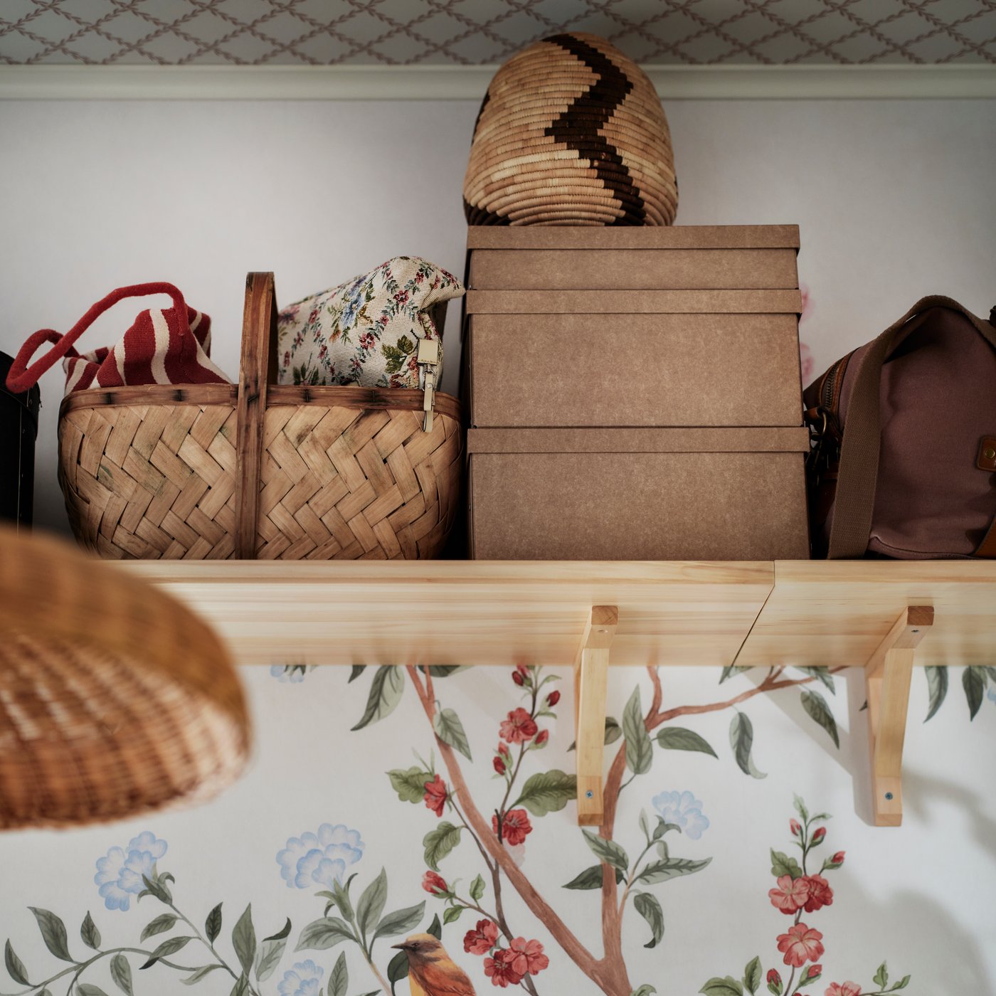 The top of a wall near the ceiling has a TRANHULT aspen shelf on it holding GÄRDESGÅRD storage boxes with lid and baskets.