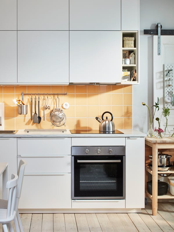 A white kitchen with white base cabinets and white wall cabinets, yellow tiles, an oven, and a wooden kitchen island.