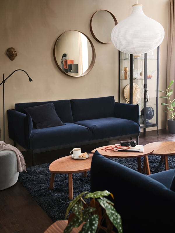 Una sala con sofás y alfombra en tonos azules. Entre los sofás hay tres mesas de madera. En una pared sobre un sofá hay dos espejos decorativos.