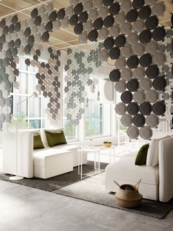 A cosy sitting area with white modular sofas and sound-absorbing panels in light and dark grey hanging from the ceiling.