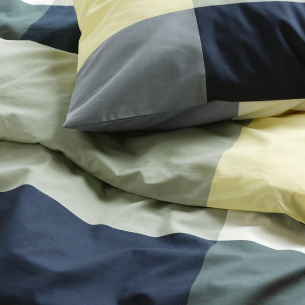 Close-up of an inviting and cosy bed with BRUNKRISSLA pastel coloured pillows and quilt cover in a large checked pattern.