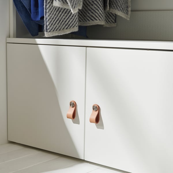 A softly sunlit PLATSA storage bench with ÖSTERNÄS leather handles on its doors. The bench stands on a light wooden floor.