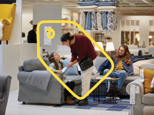 Malo dete i dve odrasle osobe u robnoj kući IKEA isprobavaju sivu sofu.