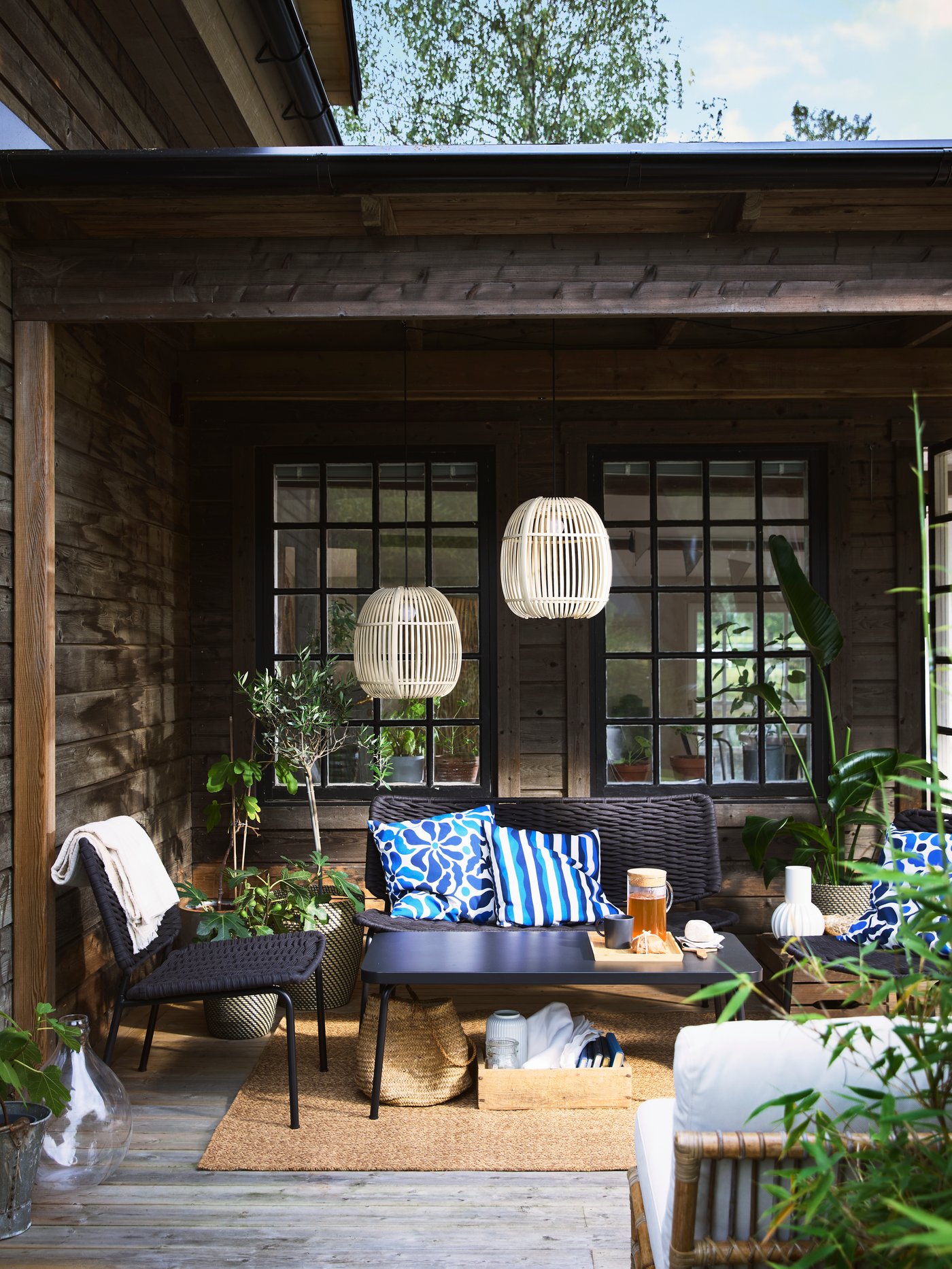 A cozy terrace with black TEGELÖN lounge furniture, blue and white pillows, and decorative SOLVINDEN lighting.