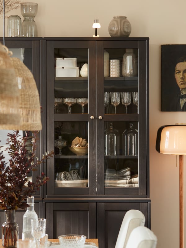 A dark brown cabinet with glass doors showing tableware and glassware inside, with integrated lighting above.