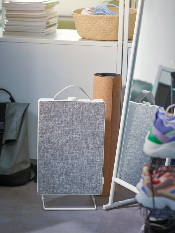 Sul pavimento, accanto a uno specchio e a un materassino per lo yoga, c'è un purificatore d'aria FÖRNUFTIG. Dietro c'è uno scaffale con libri e un cestino - IKEA.