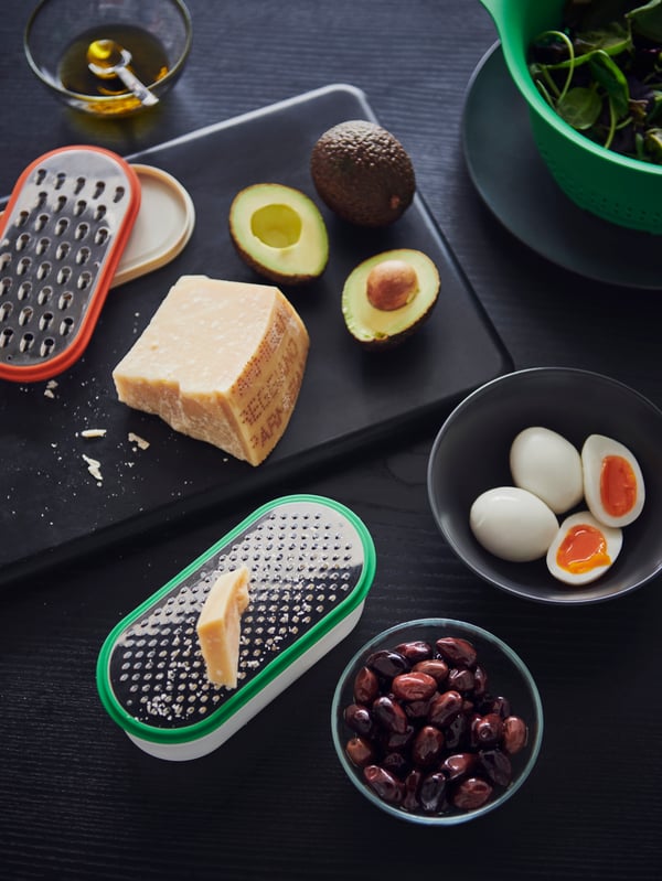 UPPFYLLD graters in different colours, some avocados and cheese and a FÄRGKLAR bowl and a GLADELIG bowl with food.