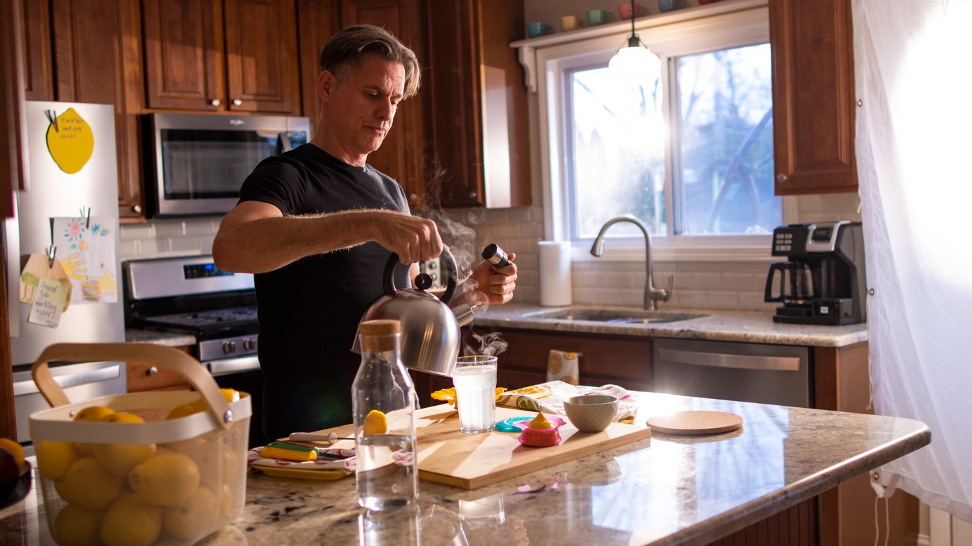 Man preparing a fresh lemon juice drink in a kitchen full of natural light.