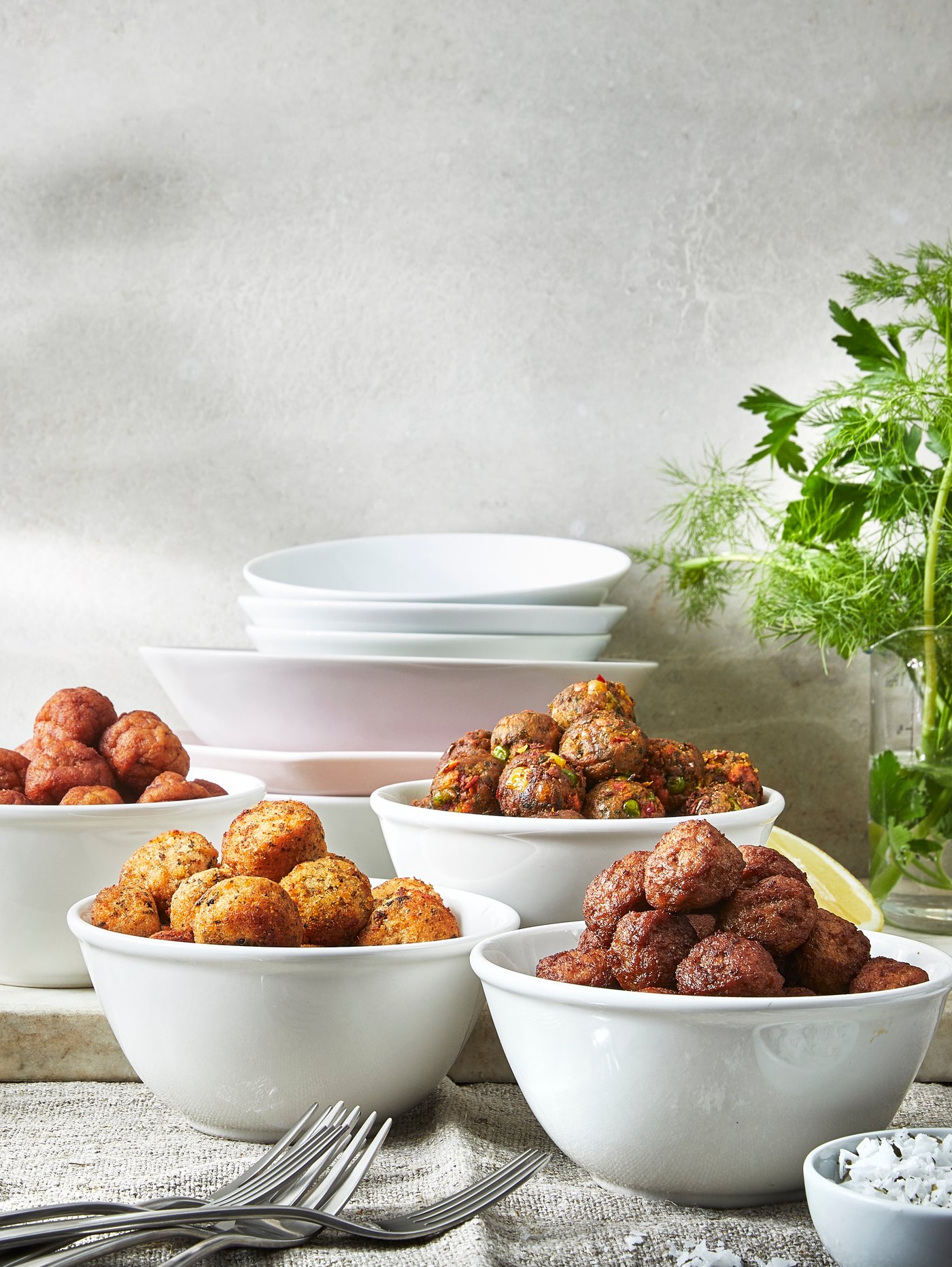 A table with four white bowls containing HUVUDROLL chicken meatballs, veggie balls, meatballs and salmon and cod balls.