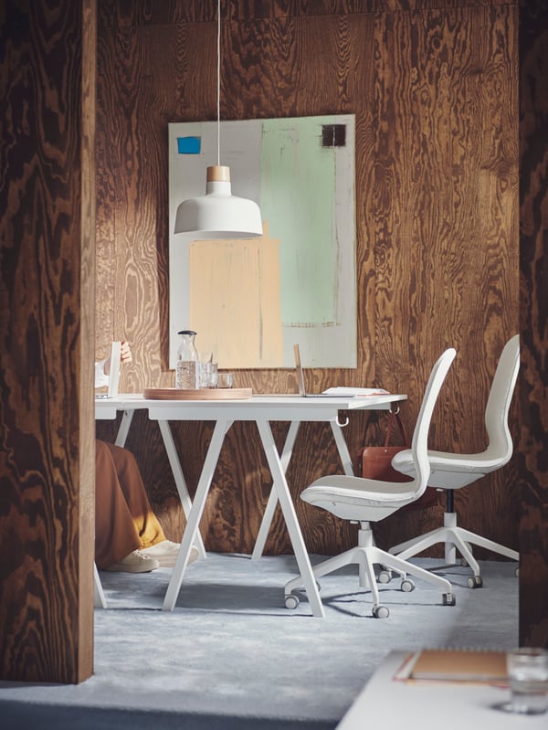 A carpeted, brown, wood-panel conference space with two white TROTTEN desks and two beige-and-white LÅNGFJÄLL office chairs.