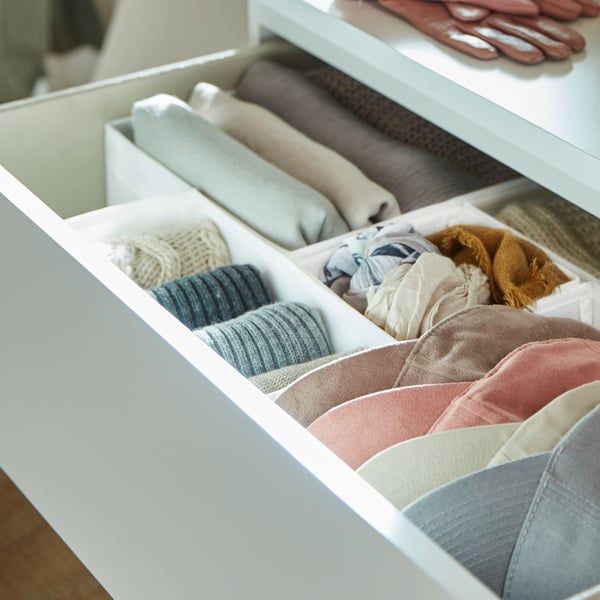The open top drawer of a  white MALM chest with 4 drawers showing small storage boxes holding small folded items inside.