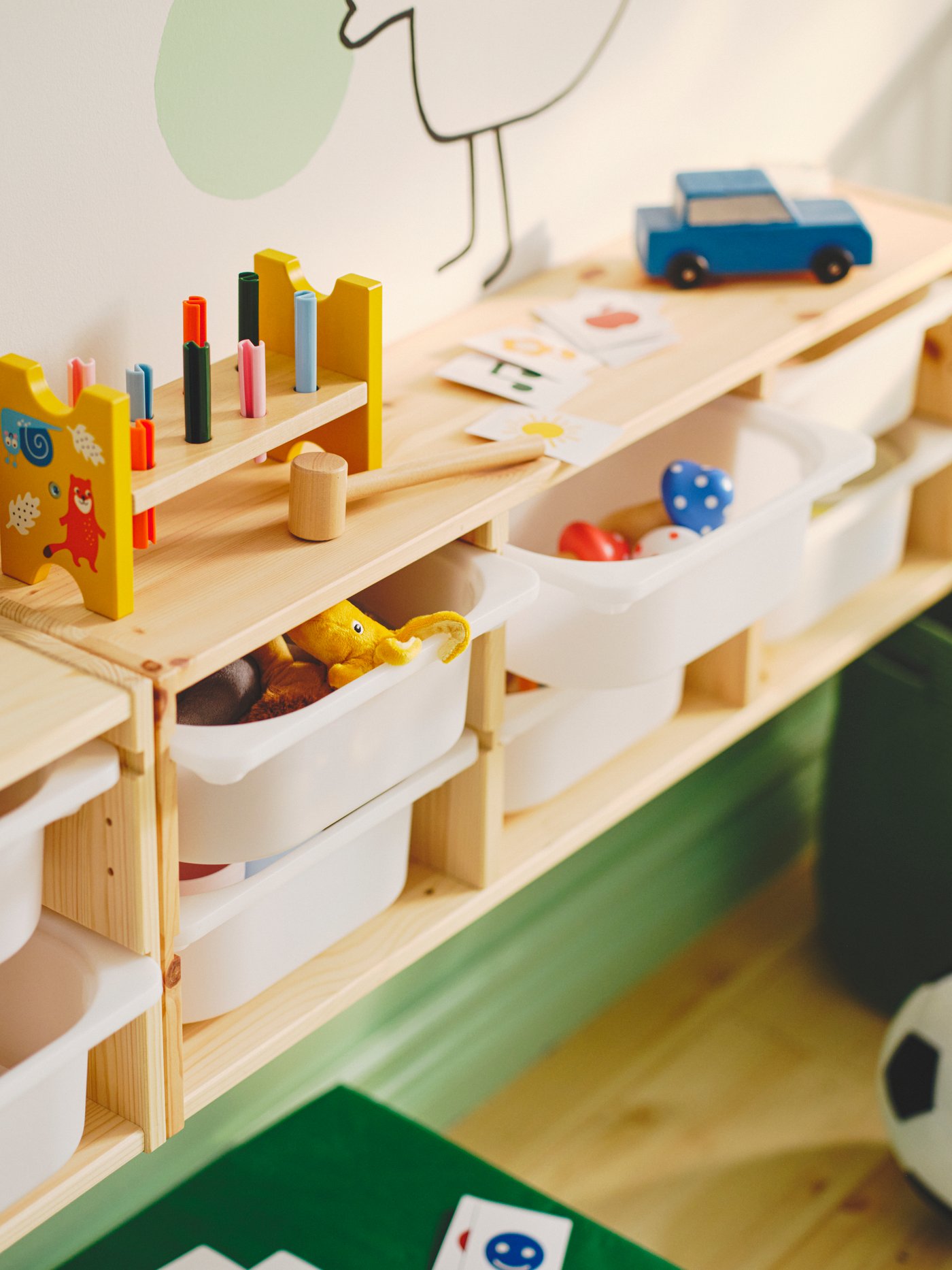 A white stained pine/white TROFAST wall storage on a wall with toys on top. Two top drawers are open showing toys inside.