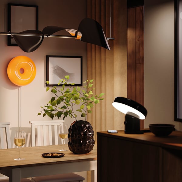 Zwarte STOCKHOLM vaas staat op een tafel in een gezellige eetruimte met verschillende lampen die een zachte sfeer creëren.