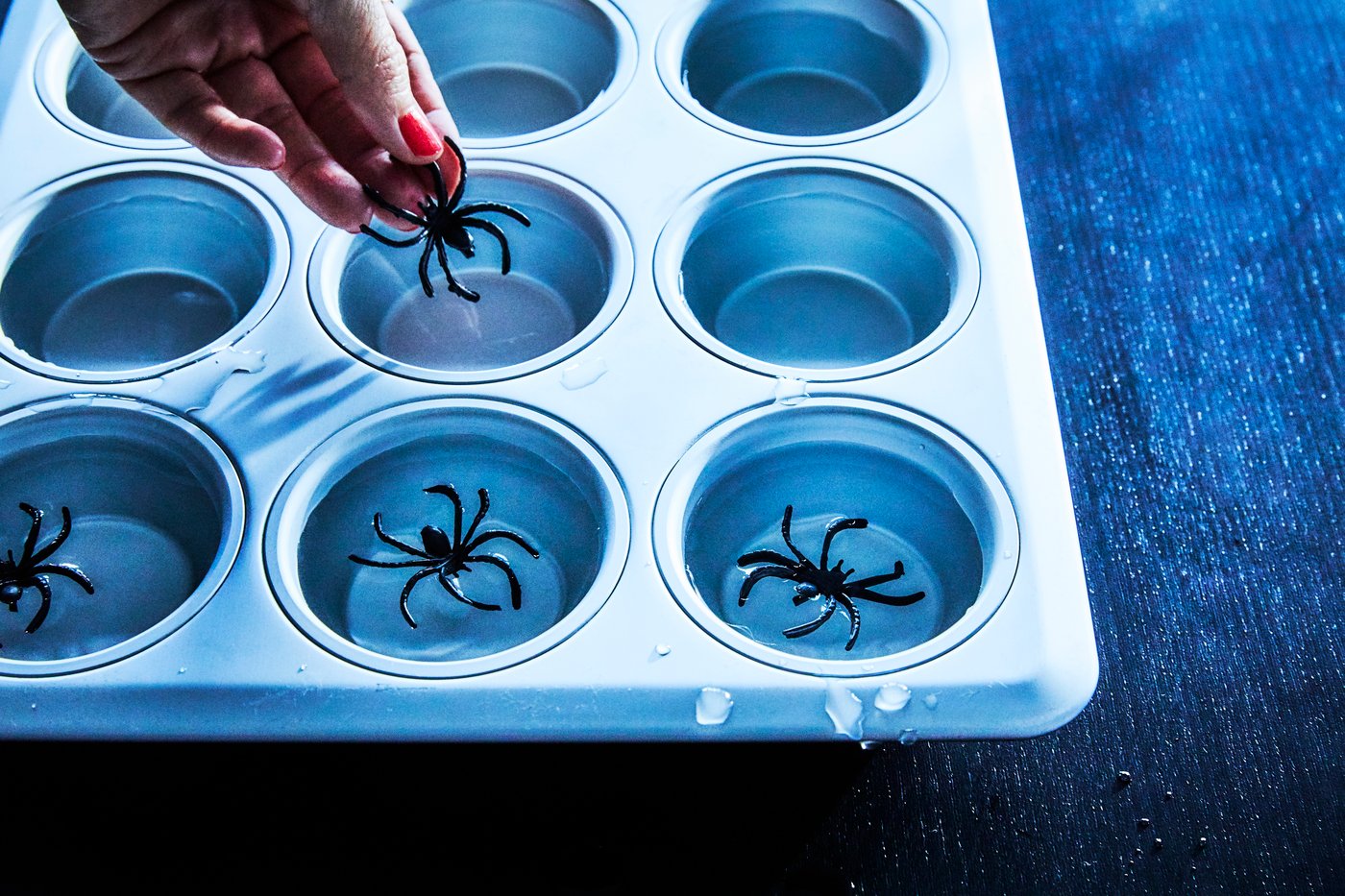 Een muffinvorm gevuld met water en plastic spinnen om ijsklontjes te maken voor Halloweenversieringen.