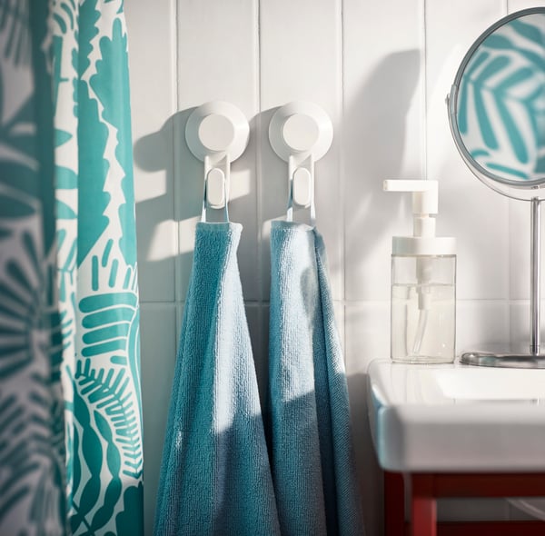 Bathroom with blue and white patterned shower curtain next to two TISKEN wall suction hooks hanging blue KORNAN towels.
