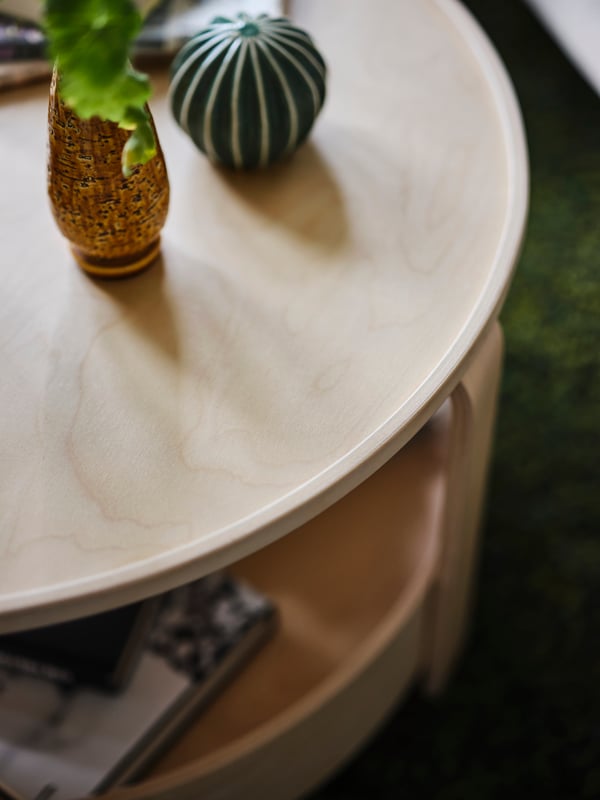 A close-up of the rounded edge of a birch veneer BORGEBY coffee table, with a vase on its surface.