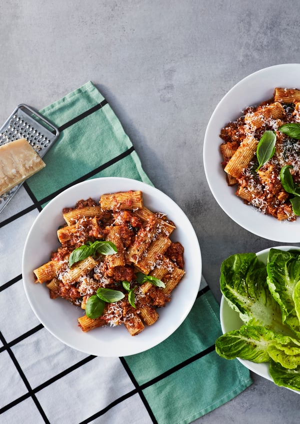 A bowl with pasta Bolognese made from HUVUDROLL plant balls minced, with fresh basil and grated parmesan, on a kitchen towel.