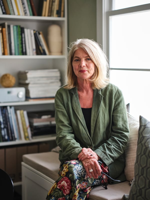 Vrouw zit op een witte PLATSA bank met opbergruimte en sierkussens, voor een witte BILLY boekenkast.