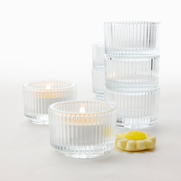 Close-up of two FINSMAK tealight holders with lit candles, next to a stack of stored tealight holders, and a pastry.
