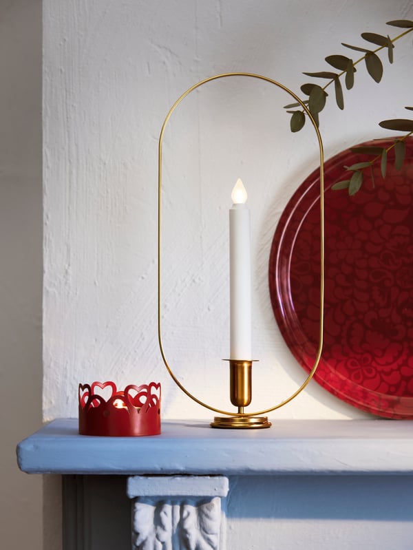 A oval brass-colour STRÅLA LED candle holder is placed on a surface beside a christmas tree dome. 