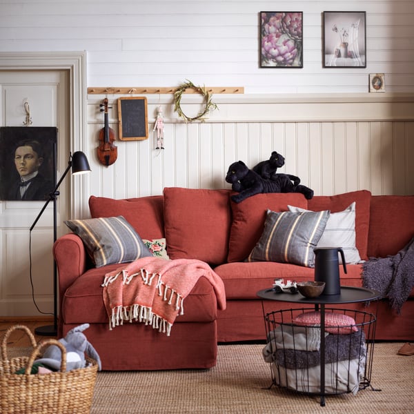 A light red GRÖNLID 3-seat sofa with chaise longue is in a rustic living room setting with soft throws and cushions.