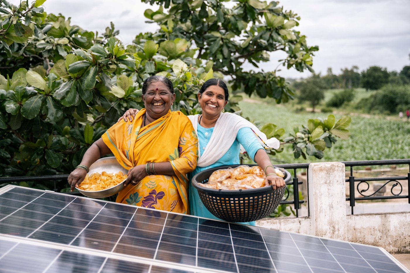 Two woman sitting behind a solar panel smiling while holding a basket
