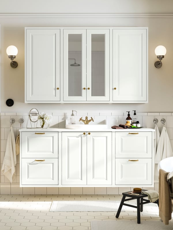 A bathroom has white TÄNNFORSEN bathroom furniture, including a vanity and a mirror cabinet with golden knobs and handles.