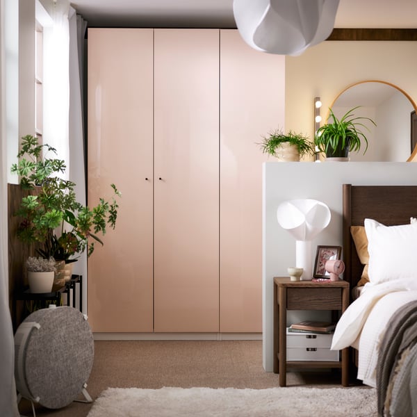 A sunny bedroom with a brown stained oak veneer TONSTAD bed in front of a PAX wardrobe with light orange FARDAL doors.