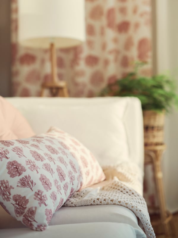 Un coussin VATTENMÅRA blanc/rose est posé sur une étoffe dans l’angle d’un canapé BACKSÄLEN 3 places blanc.