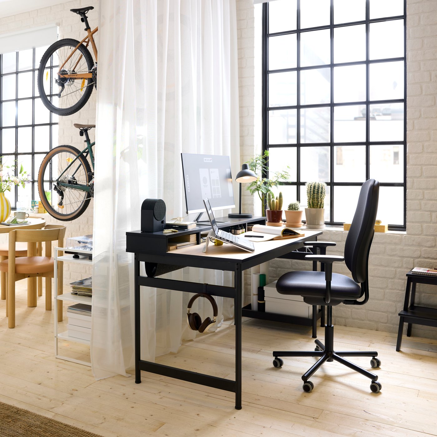 A black MULLSJÖ desk with an oak top and a black Bluetooth speaker on the top unit. In front sits a SMÖRKULL office chair.