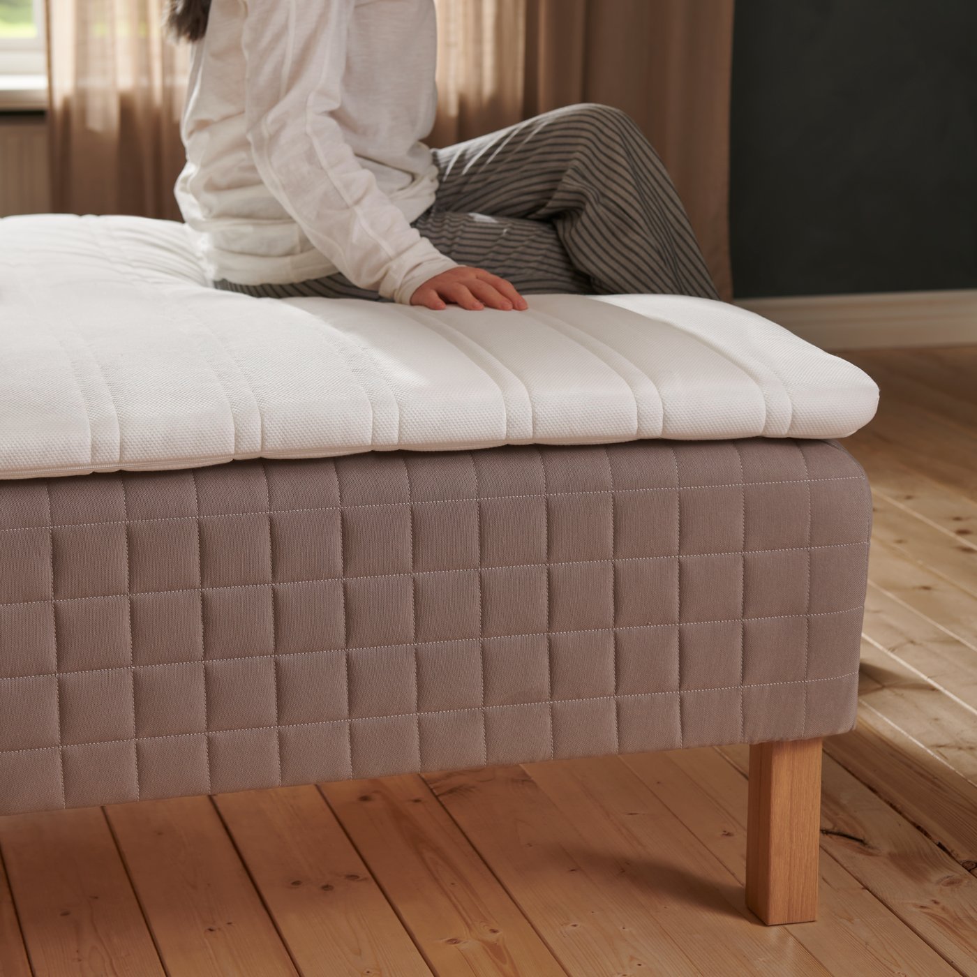 Femme assise sur un surmatelas, lui-même posé sur un sommier tapissier.
